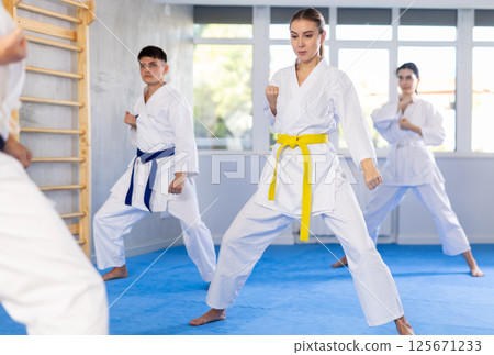 Young woman attendee of karate classes practicing kata standing in row with others 125671233