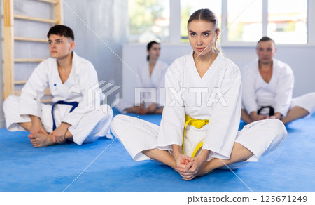 Young woman wearing kimono practicing butterfly position in sports hall Young woman wearing kimono practicing butterfly position in sports hall 125671249