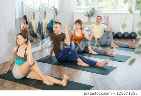 Portrait of woman sitting on sports mat and making yoga exercises with group together at fitness club 125671255