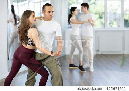 Cheerful girl and guy practicing passionate samba in dance class Cheerful girl and guy practicing passionate samba in dance class 125671321
