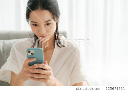 一位 30 多歲的女性正在家中操作智慧型手機 125671331