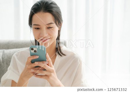 一位 30 多歲的女性正在家中操作智慧型手機 125671332