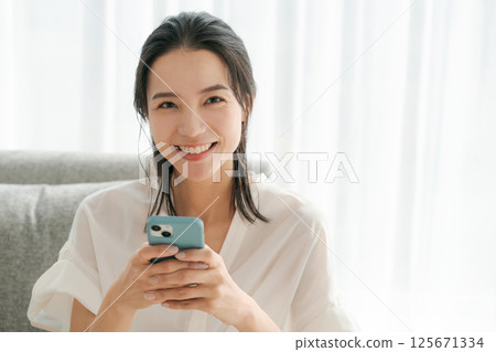 一位 30 多歲的女性正在家中操作智慧型手機 125671334