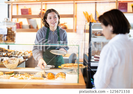 Saleswoman in an apron offers a buyer pastries 125671338