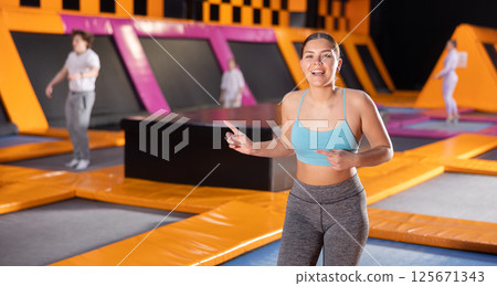 Portrait of cheerful young female in sportswear posing and smiling at camera on colorful trampoline in game club 125671343