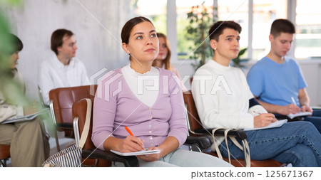 Young female student listening attentively to lecture in lecture hall Young female student listening attentively to lecture in lecture hall 125671367