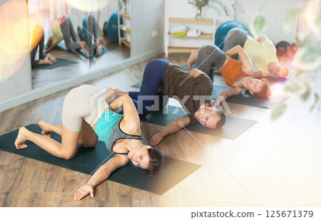 Lovers of active lifestyle on yoga mat perform doing Parivritta Eka Hasta Balasana in gym Lovers of active lifestyle on yoga mat perform doing Parivritta Eka Hasta Balasana in gym 125671379
