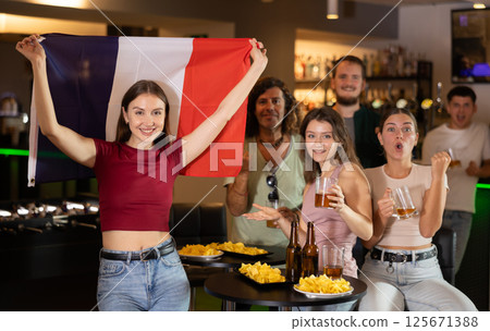Happy girl with French flag celebrates the victory of her favorite team with a group of friends in beer bar Happy girl with French flag celebrates the victory of her favorite team with a group of friends in beer bar 125671388