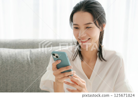 A woman in her 30s operating a smartphone at home 125671824