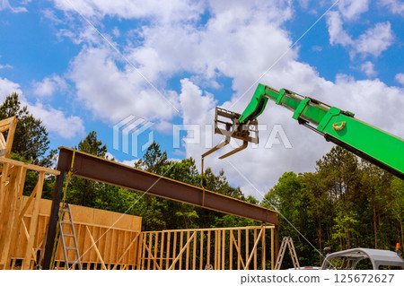 Telehandler crane carefully hoists steel beam into place at construction site while workers oversee operation. 125672627