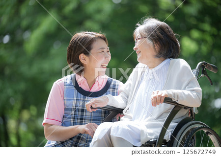 Close-up of a caregiver and an elderly person looking at each other with smiles on their faces as they take a walk in the greenery Close-up of a caregiver and an elderly person looking at each other with smiles on their faces as they take a walk in the greenery 125672749