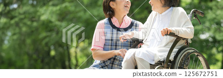 A banner of smiling caregivers and elderly people looking at each other while taking a walk in the greenery 125672751