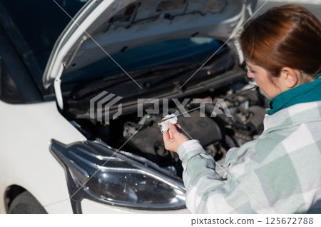 Caucasian female driver checking oil level in car engine. Caucasian female driver checking oil level in car engine. 125672788