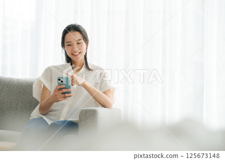 A woman in her 30s operating a smartphone at home 125673148