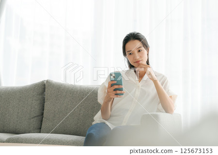 A woman in her 30s operating a smartphone at home 125673153