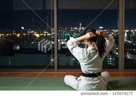 Back view of a woman sitting in a karate dojo and tying her hair up 125674277