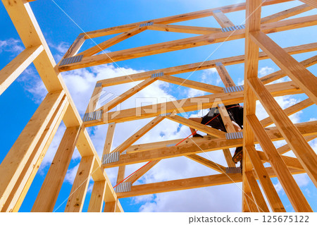 Construction worker engages in building wooden roofing frame structure, utilizing tools 125675122