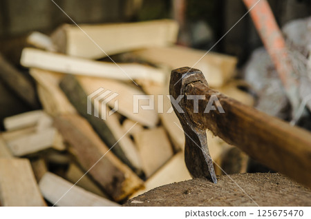 An axe stands firmly in a tree stump. Stacks of firewood fill the background. An axe stands firmly in a tree stump. Stacks of firewood fill the background. 125675470