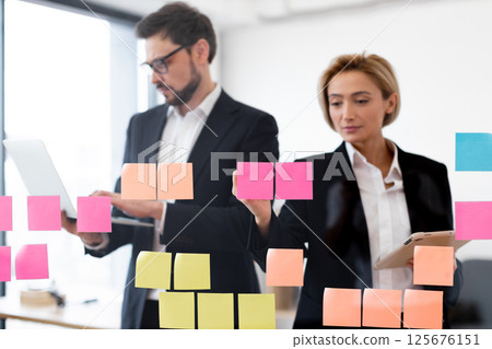 Colleagues working together on project organization using sticky notes on glass surface Colleagues working together on project organization using sticky notes on glass surface 125676151