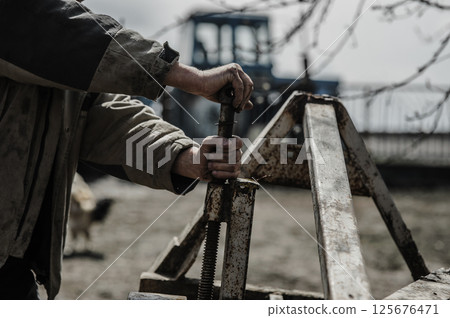 A pensioner repairs a trailer for a tractor. His hands shake from exhaustion.  125676471
