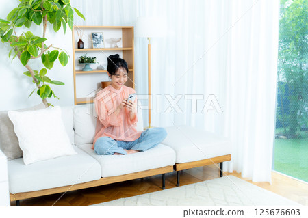 在房間裡操作智慧型手機的年輕女子 在房間裡操作智慧型手機的年輕女子 125676603