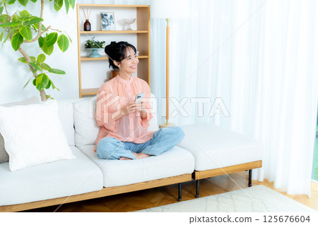 在房間裡操作智慧型手機的年輕女子 在房間裡操作智慧型手機的年輕女子 125676604