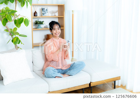 A young woman operating a smartphone in a room 125676606