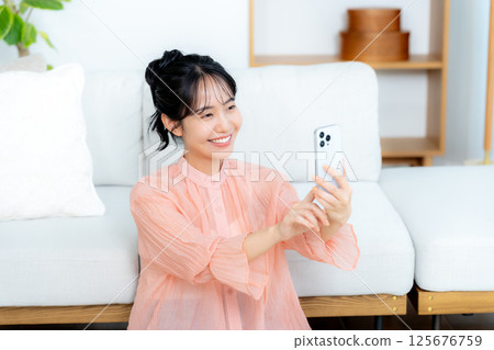 A young woman operating a smartphone in a room 125676759
