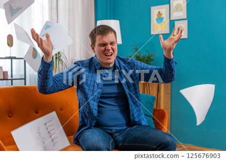Stressed angry man freelancer reviewing failure mistake charts and graphs and throwing papers in air Stressed angry man freelancer reviewing failure mistake charts and graphs and throwing papers in air 125676903