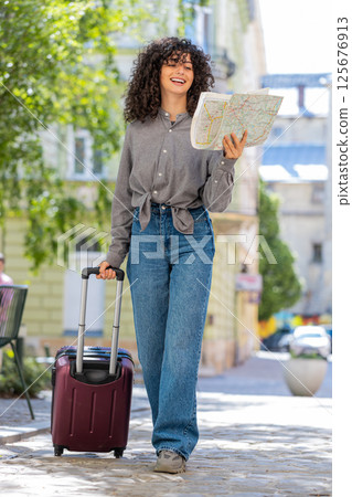 Woman tourist with suitcase exploring checking paper map search a way direction while traveling Woman tourist with suitcase exploring checking paper map search a way direction while traveling 125676913