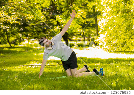 Fit flexible man doing workout yoga stretching on a sports mat in park raising arms exercising 125676925