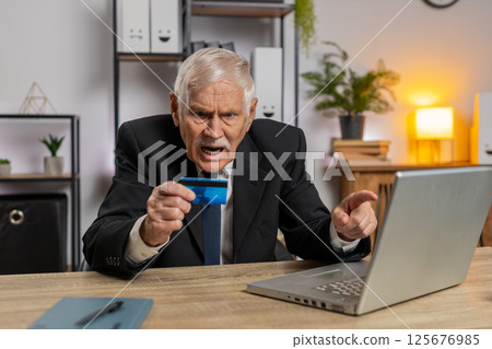 Caucasian angry senior businessman trying to pay online with smartphone blocked credit card at home 125676985