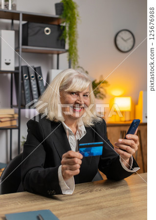 Happy Caucasian senior woman using credit card and smartphone for online shopping payments at office 125676988