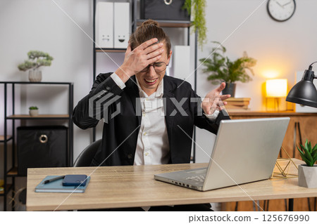 Sad businessman using laptop loses becoming surprised sudden lottery results at home office desk Sad businessman using laptop loses becoming surprised sudden lottery results at home office desk 125676990