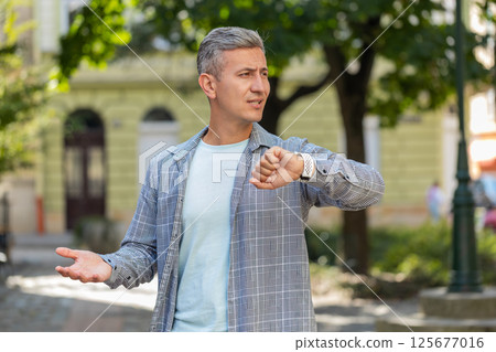Mature man looking at wristwatch while waiting for someone feeling upset about being late in city 125677016