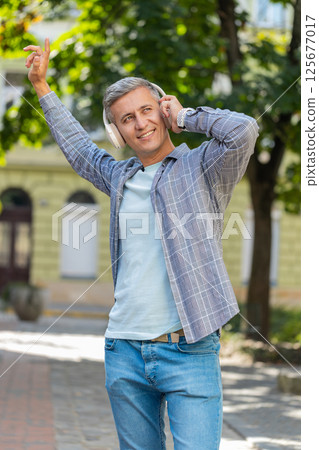 Young gray-haired man listening to music using wireless headphones and smartphone on city street Young gray-haired man listening to music using wireless headphones and smartphone on city street 125677017