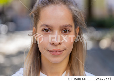 Closeup portrait of young Caucasian woman tourist teenager smiling looking at camera on city street Closeup portrait of young Caucasian woman tourist teenager smiling looking at camera on city street 125677331