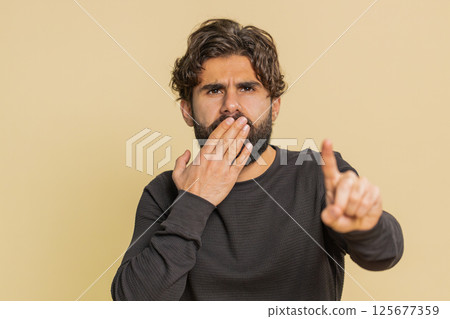 Frightened young man closing mouth with hands refusing to tell terrible secret on beige background Frightened young man closing mouth with hands refusing to tell terrible secret on beige background 125677359