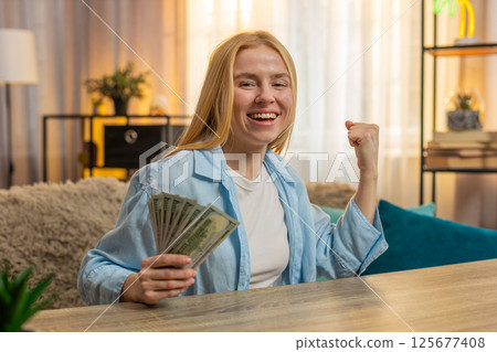 Young woman winning lottery at home table, money bundle, laughter, big joy, lucky moment, happy Young woman winning lottery at home table, money bundle, laughter, big joy, lucky moment, happy 125677408