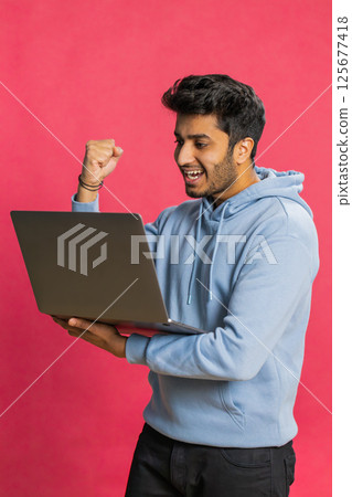 Excited happy Indian man working on laptop winning online lottery game, celebrating success, victory 125677418