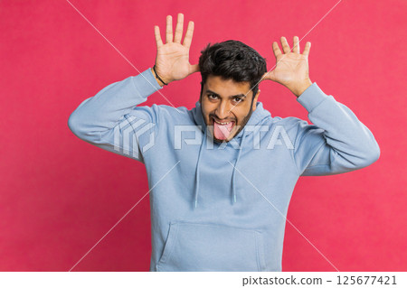 Funny comical Indian man making silly facial expressions, grimacing, fooling around, showing tongue Funny comical Indian man making silly facial expressions, grimacing, fooling around, showing tongue 125677421
