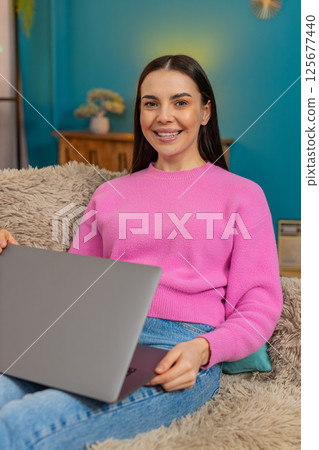 Young woman typing on laptop then closing device satisfied leaning back on sofa smiling successfully 125677440