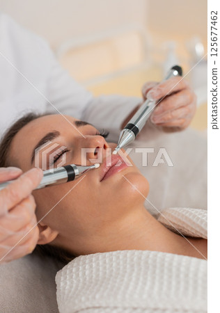 Caucasian young woman gets lips zone facial therapy with modern device by cosmetologist in clinic Caucasian young woman gets lips zone facial therapy with modern device by cosmetologist in clinic 125677462