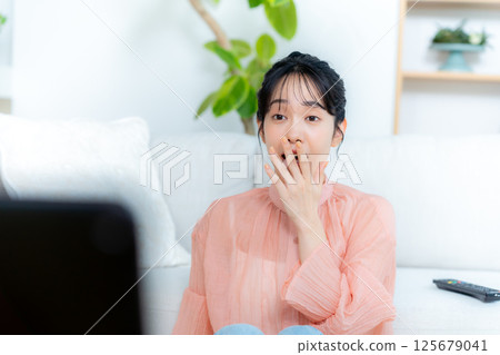 一位年輕的女士在客廳裡看電視 125679041