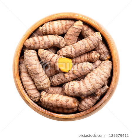 Fresh turmeric rhizomes in wooden bowl. Underground stems of the turmeric plant Curcuma longa. One stem is cut open, showing the bright orange flesh. Used fresh or dried and ground as turmeric powder. 125679411