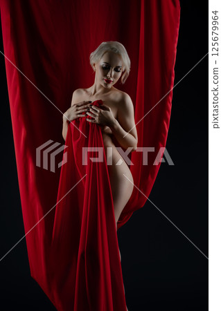 Woman poses gracefully with red fabric in artistic studio setting 125679964
