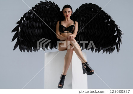 Beautiful woman in black lingerie with striking wings poses elegantly indoors 125680827