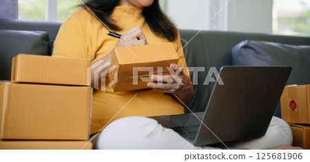 Mature business owner woman prepare parcel box and standing check online orders for deliver to customer on tablet, laptop Shopping Online 125681906