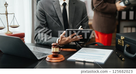 justice and law concept.law theme wooden desk, books, balance. Male judge in a courtroom the gavel,working with digital tablet computer on table 125682023