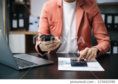 Businessman hands working with finances about cost and calculator and laptop with tablet, smartphone at office in morning light 125682096
